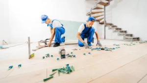Zwei Fachkräfte in blauen Overalls arbeiten an der Installation eines Holzbodens. Böden verlegen